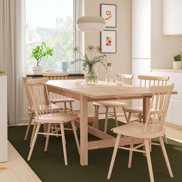 Installation moderne de salle à manger KARSKÄR avec table extensible et six chaises à fuse. La décoration comprend un vase avec des fleurs et des illustrations murales, à côté de la cuisine.