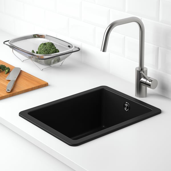 Évier de cuisine moderne avec robinet métallique, contenant des légumes verts frais dans une passoire à côté.