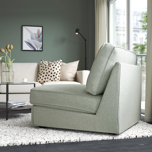 Salon moderne avec murs végétaux. Le canapé-lit gris est positionné près d’une grande fenêtre. Une table basse blanche avec des livres et des fleurs se trouve à côté.