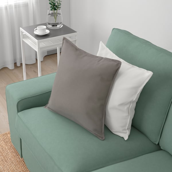 Un canapé vert avec des oreillers gris et blancs se trouve près d’une table blanche avec une plante et des tasses.