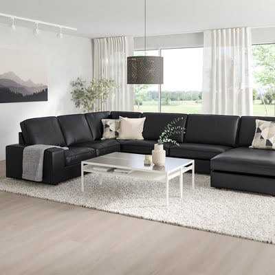 Salon moderne avec grand canapé sectionnel KIVIK noir, table basse blanche et grandes fenêtres. Design élégant et minimaliste pour la détente.
