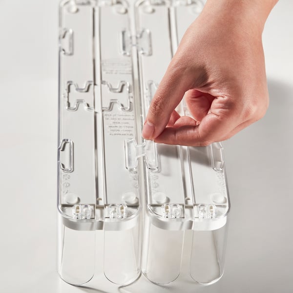 La main tient l’organisateur de boissons en plastique transparent, ajustant la largeur des bouteilles, assurant un rangement soigné dans le réfrigérateur.