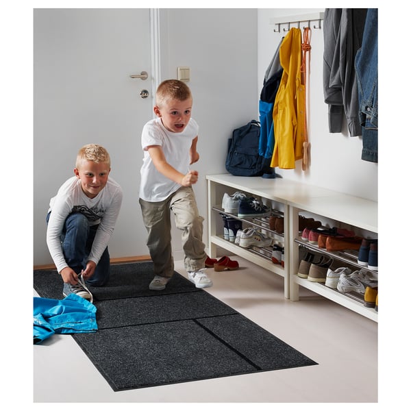 Des enfants jouent dans une entrée lumineuse avec un tapis KÖGE, un porte-chaussures et des vestes suspendues.