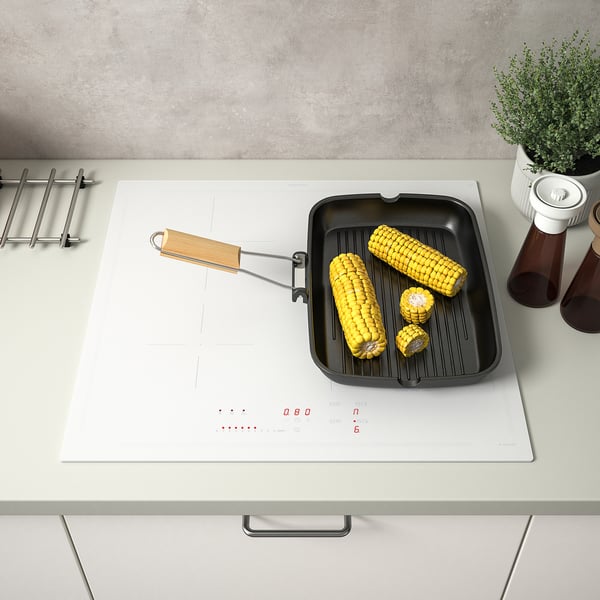 Une cuisinière à induction avec des commandes tactiles cuit des épis de maïs. Le réchaud a une fonction de pont, reliant deux zones de cuisson en une seule.
