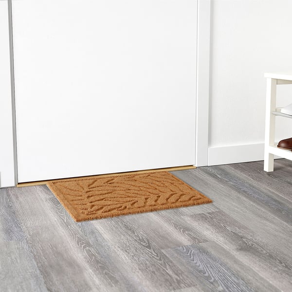 Paillasson avec motif de feuilles en relief à l’entrée, piège efficacement la saleté.