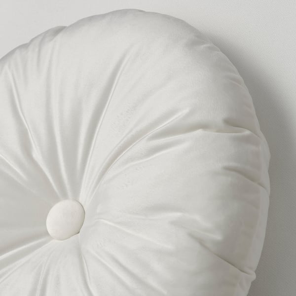 Coussin blanc rond et luxueux avec une texture lisse et veloutée sur un couvre-lit léger.