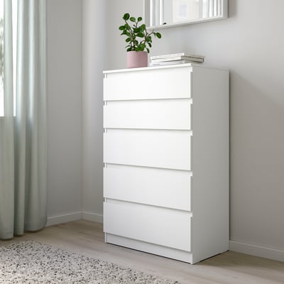 Commode KULLEN blanche dans le coin de la chambre, avec des livres et des plantes, des tiroirs hauts et larges.