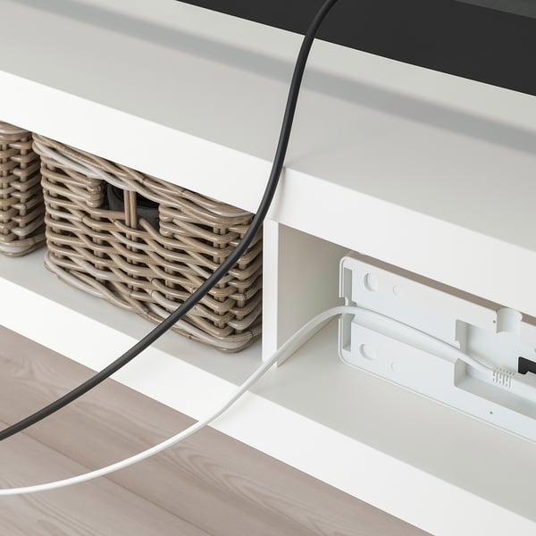 Un banc TV LACK blanc avec des paniers tressés et un système de gestion des câbles visible derrière.
