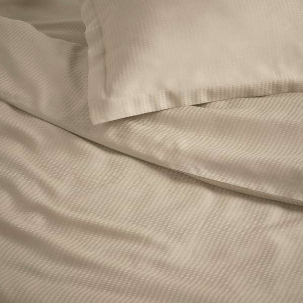 Parure de lit ivoire soigneusement pliée avec un motif de tissage subtil. Texture douce et lisse, suggérant un matériau confortable de haute qualité.