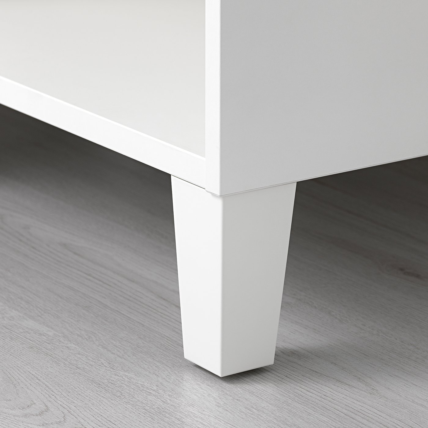 Gros plan d’un pied de meuble blanc au design épuré et élégant, monté sur un plancher en bois, présentant une finition de haute qualité.