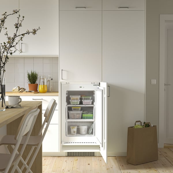 Scène de cuisine : réfrigérateur-congélateur ouvert avec tiroirs transparents à l’intérieur, placé sous l’armoire.