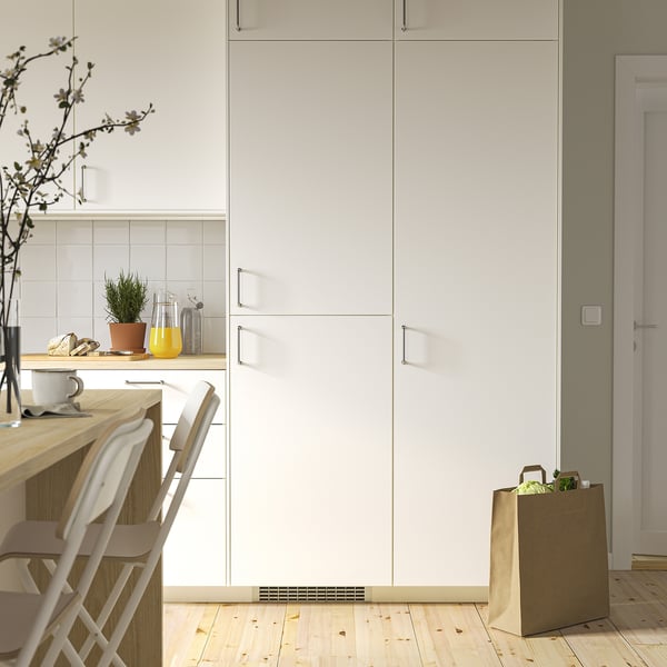 Réfrigérateur blanc moderne encastré dans les armoires de cuisine, plus petit que les chaises et les articles de comptoir adjacents.