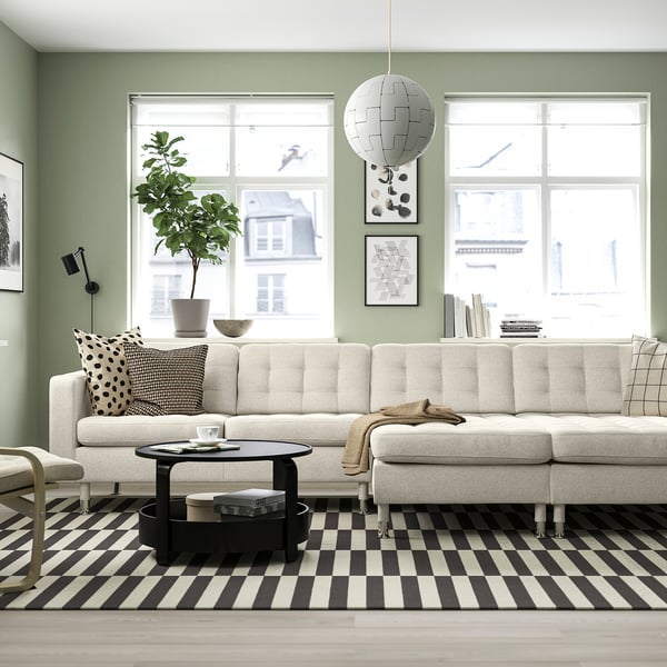 Salon moderne avec canapé en forme de L, tapis noir/blanc, table basse ronde, suspension et décor minimaliste.