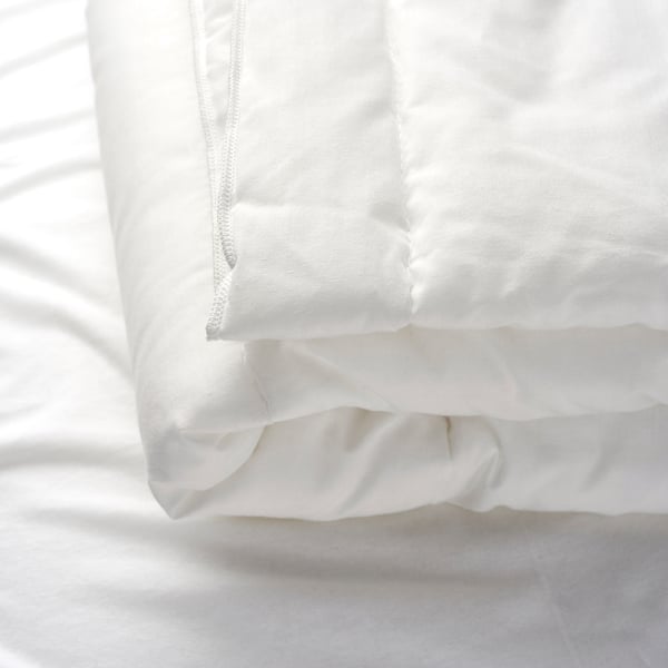 Gros plan d’une couette blanche douce et ultra-moelleuse avec des coutures visibles et une texture propre et légère.