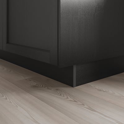 Socle d’armoire de cuisine noir couvrant l’espace au sol, montré sur le plancher en bois.
