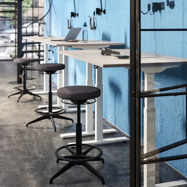 Bureau moderne avec tabourets LIDKULLEN, sièges gris et circulaires, bureaux hauts réglables et murs bleus.