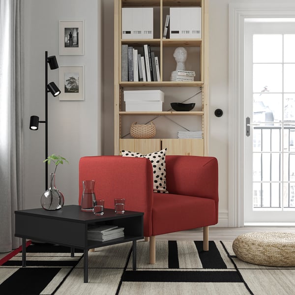 Salon moderne avec canapé en lillem rouge, table basse noire, tapis noir et blanc, étagère en bois et lampadaire noir.