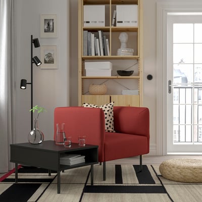 Salon moderne avec canapé rouge, étagère, table basse, tapis, lampe et lumière naturelle.