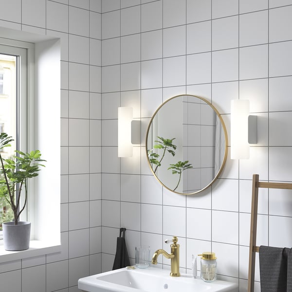 Salle de bain moderne avec miroir doré, lavabo, lumières, plante et serviettes.