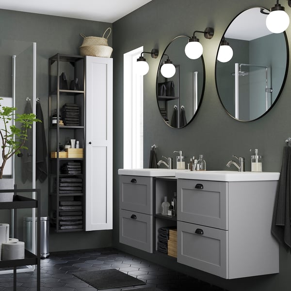 Salle de bain moderne avec miroirs ronds noirs, armoires grises, comptoir blanc, film de sécurité.