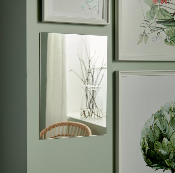 Miroir sur mur vert au milieu d’œuvres d’art encadrées. Reflète la chaise et les branches.