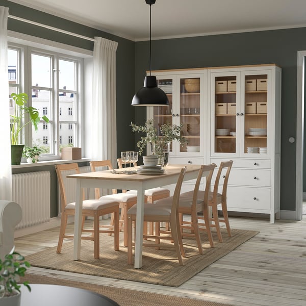 Salle à manger avec tapis en jute LOHALS , table blanche et chaises. Grande fenêtre avec rideaux, armoire blanche avec vaisselle. Le tapis est durable et à plat.