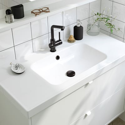 Lavabo de salle de bain moderne avec robinet noir élégant, comptoir blanc et accessoires, y compris un distributeur de savon et une plante.