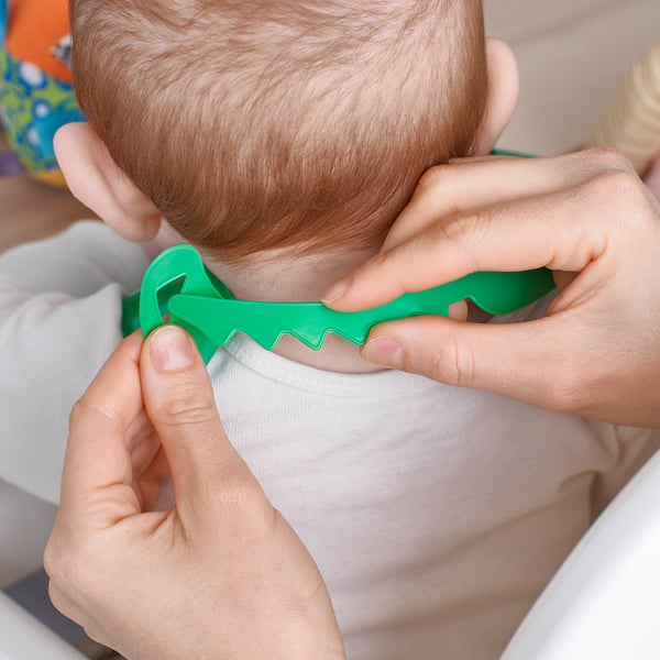 Le bavoir pour bébé avec sangle de cou réglable est fixé par des mains d’adultes, ce qui permet de retenir les éclaboussures pendant les repas.