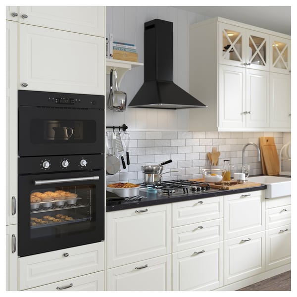 Cuisine moderne avec four double, cuisinière noire élégante, armoires blanches, ustensiles en bois et ustensiles de cuisine suspendus.