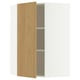 Une armoire d’angle METOD ouverte avec une finition en chêne clair. Il s’agit d’une porte et d’étagères en panneaux de particules et de fibres de bois avec un design moderne et minimaliste.
