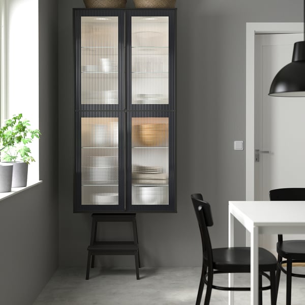 Cuisine moderne ikea METOD noire avec armoire à portes vitrées et plante.