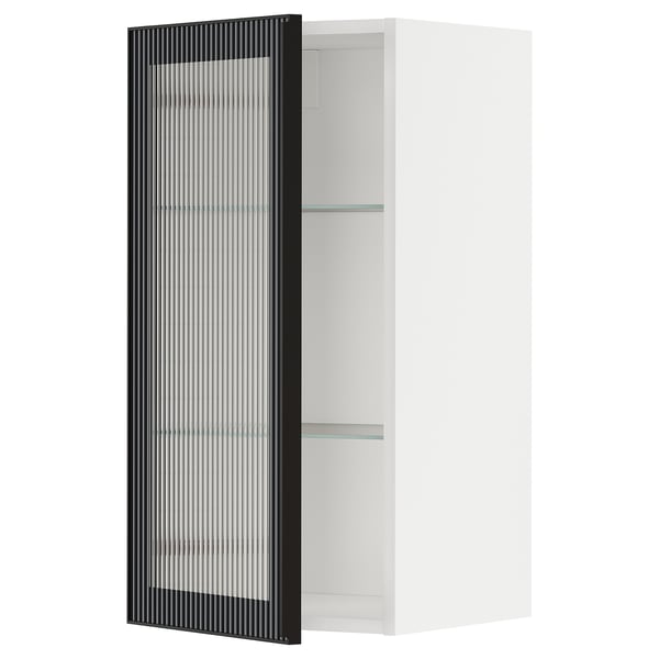 Il s’agit d’une armoire de cuisine METOD blanche avec une porte en verre hejsta noire avec du verre dépoli et un cadre métallique, offrant un aspect moderne.