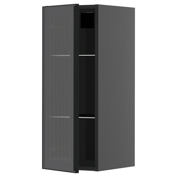 Une armoire de cuisine moderne noire avec une porte en verre dotée d’un cadre en métal et d’un design de roseaux verticaux, faisant partie du système METOD.