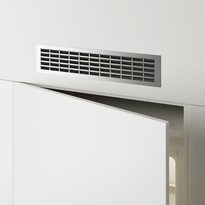 Grille de ventilation rectangulaire en métal montée sur un mur blanc au-dessus d’une porte, permettant la circulation de l’air.