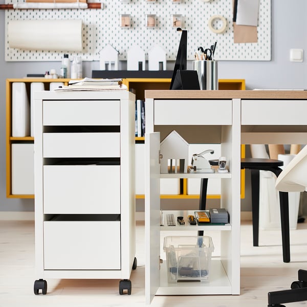 Bureau blanc moderne avec tiroirs et étagères, avec des fournitures soigneusement rangées et une décoration en forme de maison.