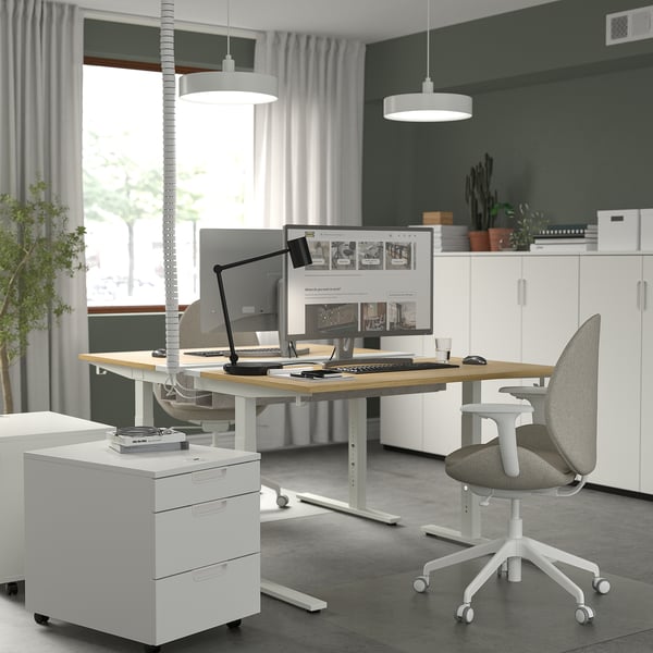 Bureau réglable en hauteur avec 2 écrans, ordinateur portable, chaise ergonomique, rangement, fenêtre, lumières.