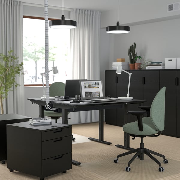 Configuration du bureau à domicile avec un bureau noir réglable en hauteur MITTZON , des chaises vertes et des armoires noires, avec une grande fenêtre et des lumières suspendues.