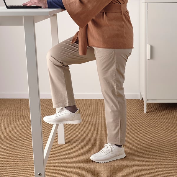 Debout à un bureau, genou sur un repose-pieds, ordinateur portable. Espace de travail bien rangé pour assis/debout.