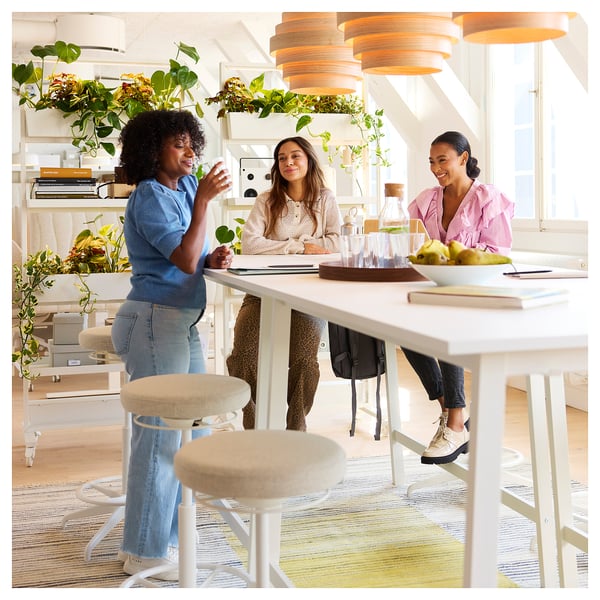 Trois femmes collaborent autour d’une table MITTZON moderne avec gestion des câbles dans une pièce lumineuse et remplie de plantes.