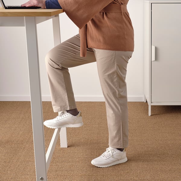 Personne debout à une table haute avec repose-pieds intégrés, favorisant un travail ergonomique en position assise ou debout.