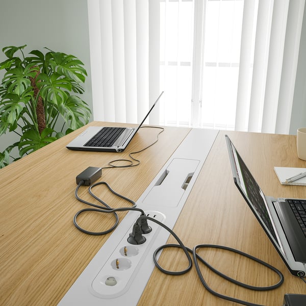 Table de bureau avec ordinateurs portables et multiprises, avec gestion des câbles et une plante.