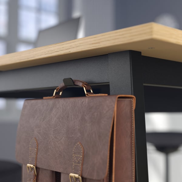 Le sac en cuir marron est suspendu à un crochet en métal noir, relié à une étagère en bois, s’adaptant à la décoration du bureau.