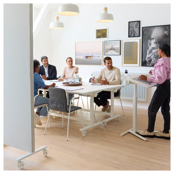 Bureau moderne : cinq personnes à des tables MITTZON blanches, une debout, d’autres assises. Art sur les murs, parquet clair, configuration de réunion confortable.