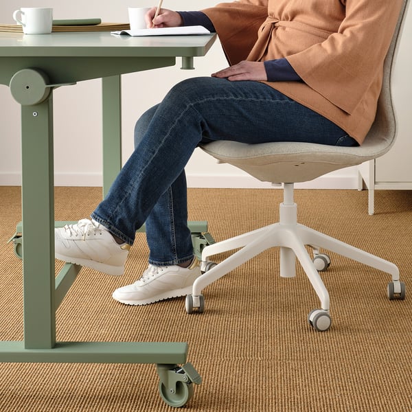 La personne est assise à un bureau réglable sur une chaise ergonomique avec repose-pieds, notes à la main.
