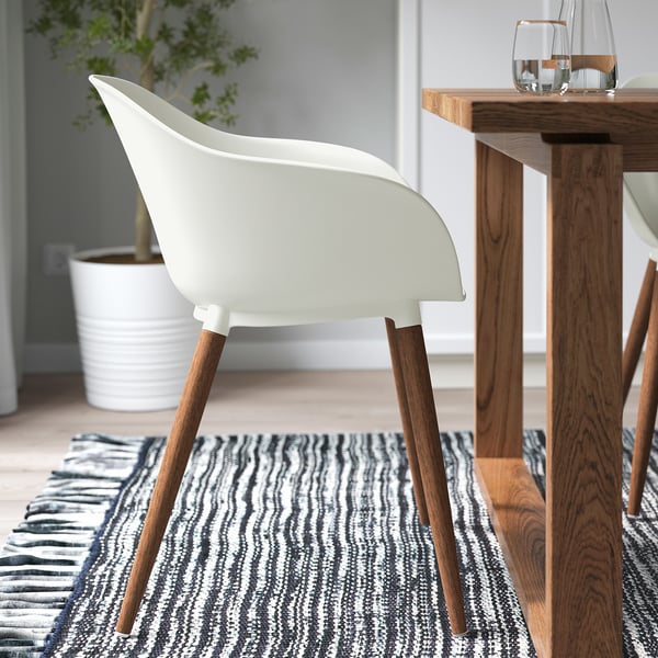 Chaise blanche avec pieds en bois à la table à manger sur un tapis rayé.