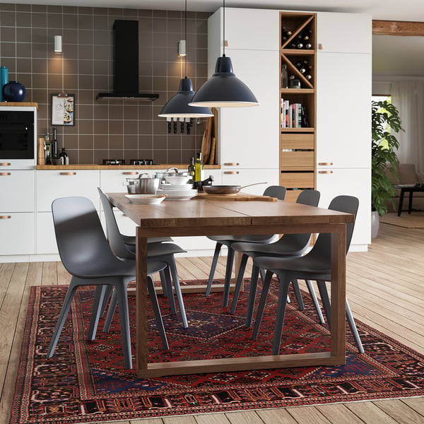 Cuisine moderne avec table à manger en chêne MÖRBYLÅNGA, chaises grises, suspensions noires, armoires blanches et tapis rouge foncé.