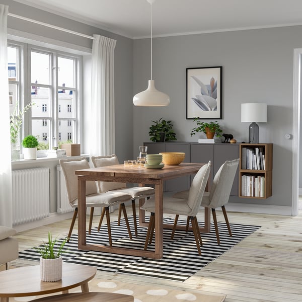 Salle à manger moderne avec table en bois, chaises grises, suspension et plantes.