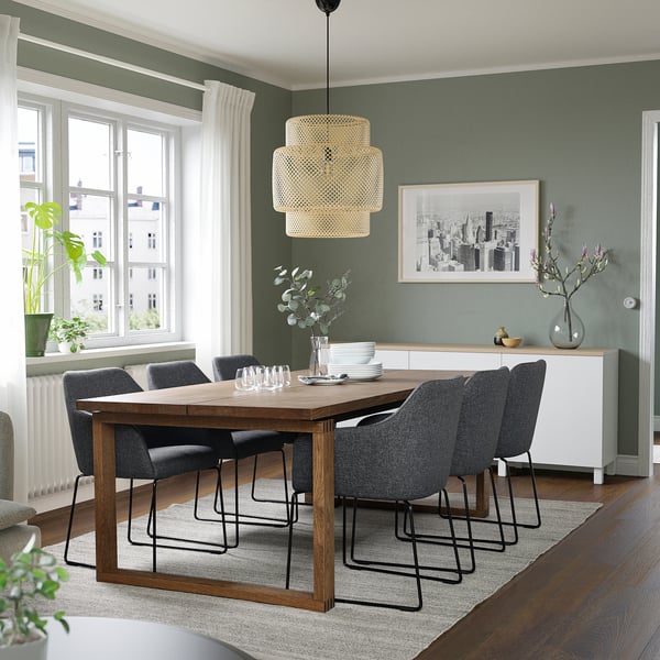 Salle à manger moderne avec table en bois, chaises grises, lampe suspendue, murs verts et photo de paysage urbain.