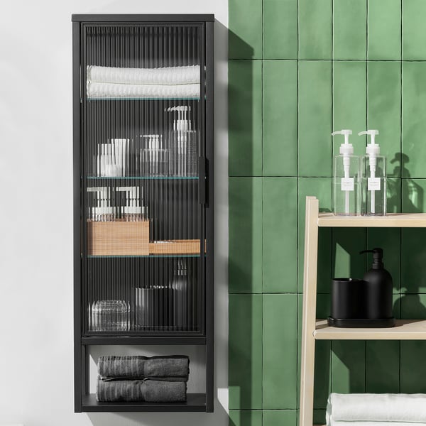 Armoire MOSSJÖN noire avec étagères en verre roseau, contenant des articles de toilette, des serviettes. Design moderne avec des carreaux verts.