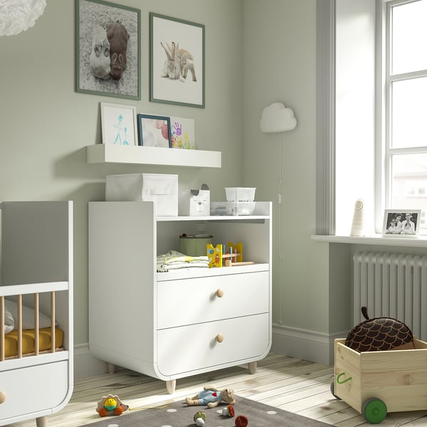 Chambre d’enfant avec commode MYLLRA, berceau, jouets, murs végétaux, tapis, lampe.